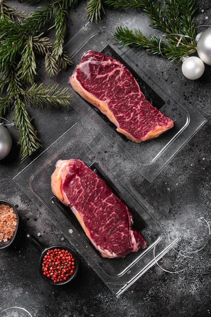 Steak de New-York emballé sous vide avec un ensemble d'arbres de Noël, sur fond de table en pierre noire foncée, vue de dessus à plat