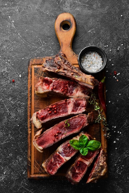 Steak à l'os sur la planche de cuisine Tomahawk steak sur fond de bois noir Vue de dessus Espace libre pour la copie