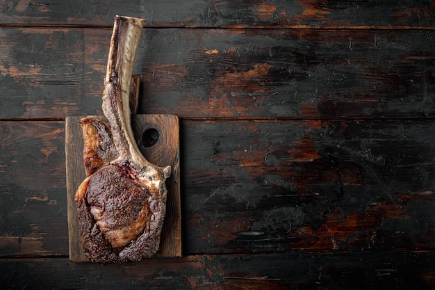 Steak sur l'os. steak de tomahawk, ensemble de nourriture pour barbecue séché et grillé, sur une planche de service en bois, sur un vieux fond de table en bois sombre, vue de dessus à plat, avec espace de copie pour le texte