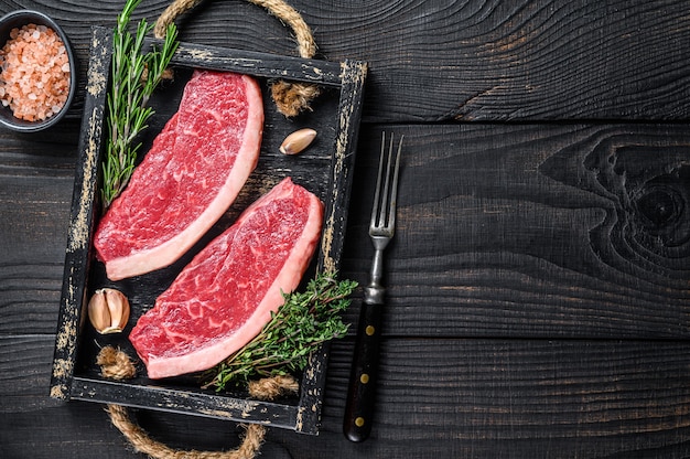 Steak de picanha brésilien cru ou steak de viande de boeuf de surlonge dans un plateau en bois. Fond en bois noir. Vue de dessus. Espace de copie.