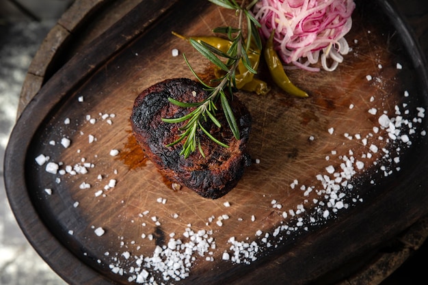 Un steak sur une planche de bois avec un tas de sel et de poivre dessus.