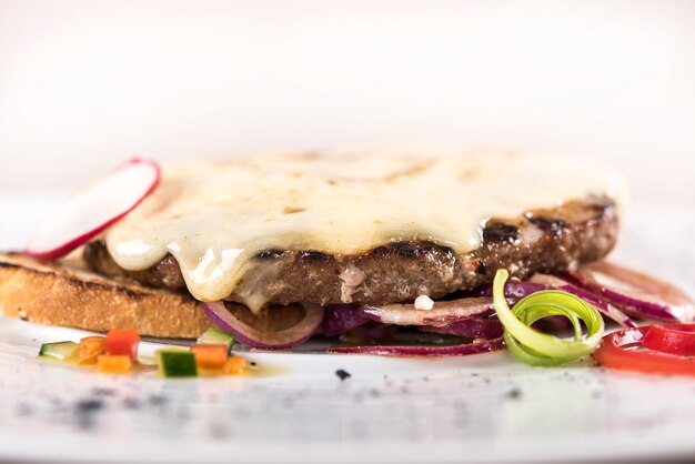 Steak de porc au fromage, posé sur du pain grillé et de l&#39;oignon rouge, décoré de feuilles vertes et rouges