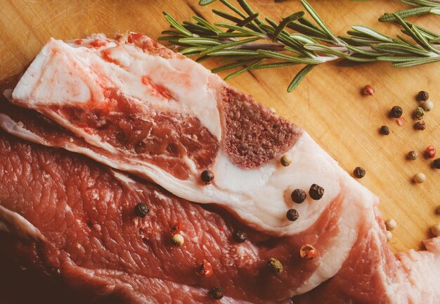 Steak de porc au romarin et au poivre sur un fond en bois Steak de viande crue traitement photo vintage