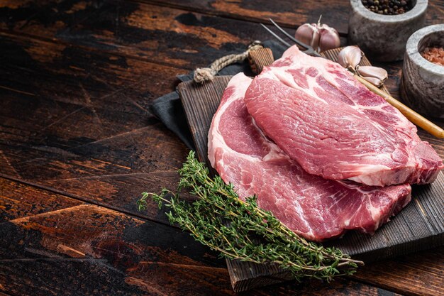 Steak de porc cru de boucher à partir de viande de filet de cou crue sur planche de bois aux herbes. Fond en bois. Vue de dessus. Espace de copie.