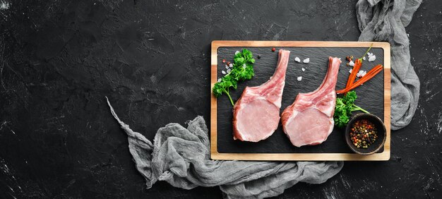 Steak de porc cru sur l'os Sur une planche de pierre avec des épices et des herbes Vue de dessus Espace libre pour votre texte