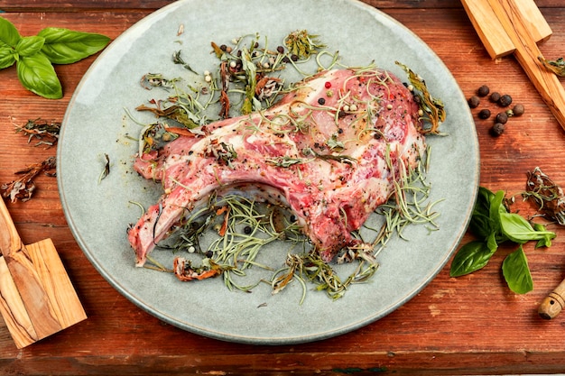 Photo steak de porc cru tomahawk mariné dans des herbes épicées avec des ingrédients pour le grillage sur fond de bois