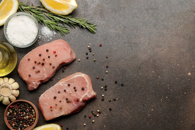 Steak de porc cru, viande et ingrédients pour la cuisson, épices, herbes et légumes sur fond sombre. vue de dessus. espace pour le texte