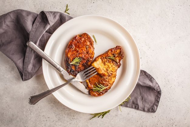 Steak de porc cuit au romarin sur une assiette blanche, vue de dessus.