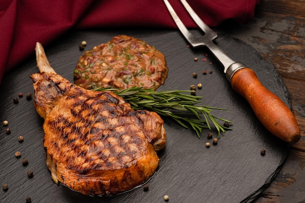 Photo steak de porc grillé au sel et poivre de romarin sur une plaque de pierre noire grillé épais juteux