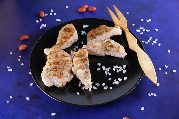 Steak de porc grillé aux épices sur fond bleu Steak de porc avec fourchette en bois et sel de mer sur une plaque noire Gros plan