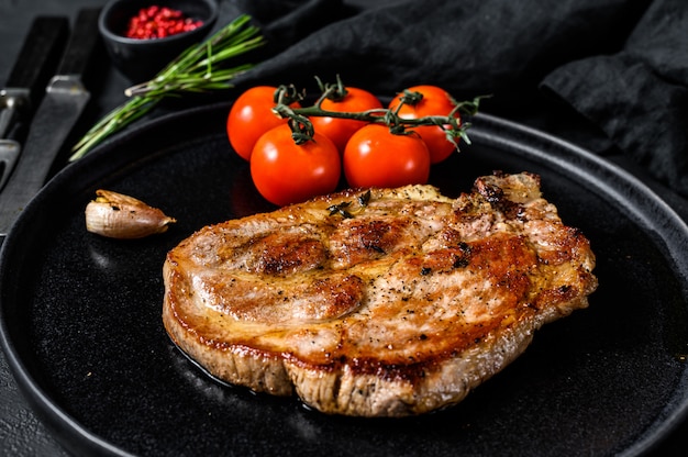 Steak de porc grillé sur os avec tomates. Fond noir. Vue de dessus