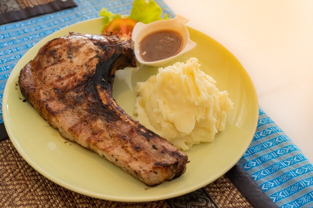 Photo steak de porc grillé servi avec purée de pommes de terre et sauce au jus dans une assiette jaune