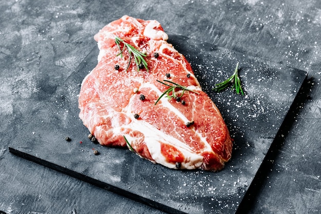 Steak de porc en marbre cru sur une planche sombre