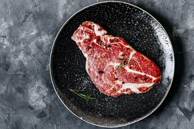 Steak de porc en marbre cru sur une vue de dessus de plaque sombre