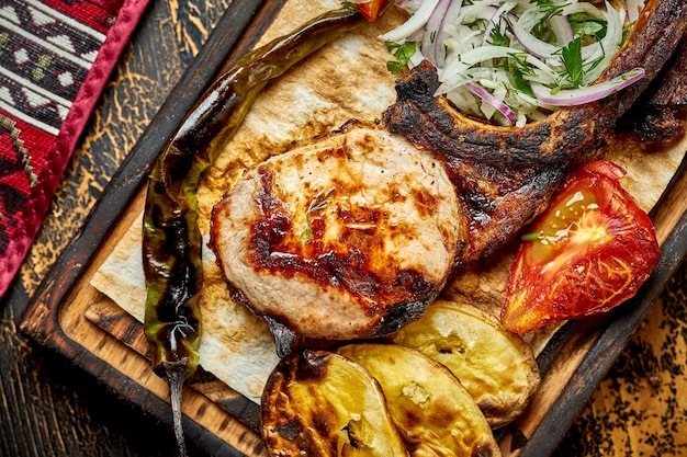 Steak de porc à l'os grillé avec des légumes sur une planche de bois Gros plan