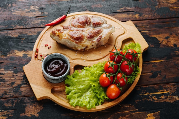 Steak de porc sur une planche en bois avec tomates cerises et salade nourriture rustique