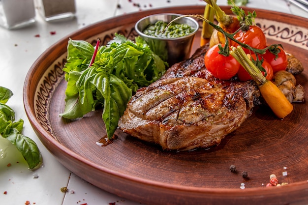 Steak de porc servi avec légumes grillés, champignons et sauce pesto