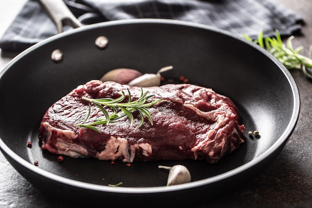 Steak de Ribe Eye de boeuf cru frais dans une poêle en téflon avec du romarin, de l'ail, du sel et du poivre.