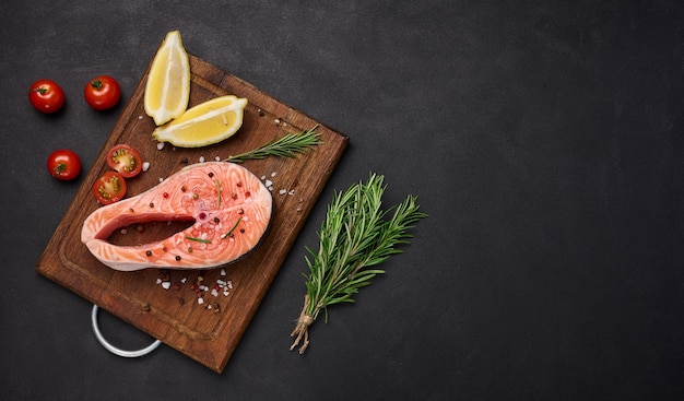 Steak de saumon cru sur une planche à découper en bois tranches de citron épices Vue de dessus sur tableau noir