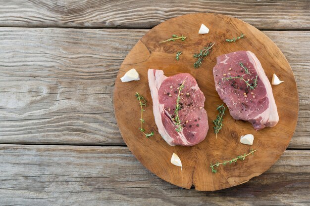 Steak de surlonge, ail et herbes sur plateau en bois contre table en bois