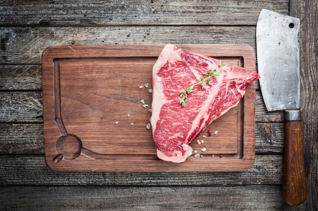 Steak de T-bone cru aux herbes fraîches et à l'huile sur fond de bois foncé, vue de dessus