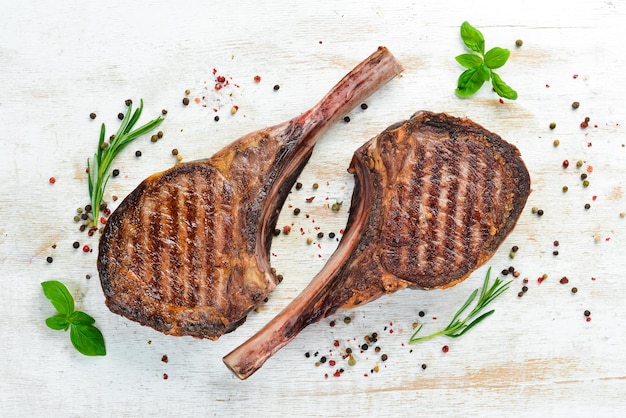 Steak de Tamahavk sur l'os avec des épices et des herbes Sur un fond en bois blanc Vue de dessus Espace de copie gratuit