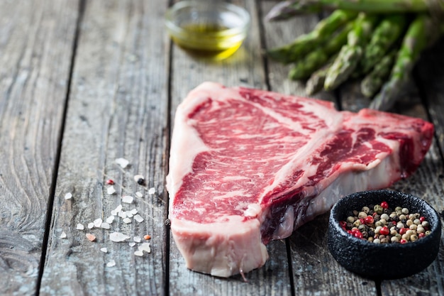 Steak de tbone cru aux herbes fraîches et à l'huile sur fond de bois foncé