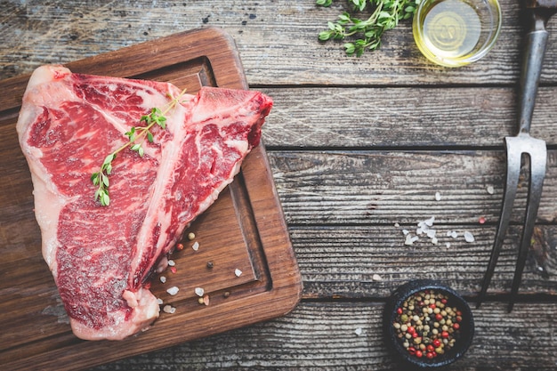 Steak de tbone cru avec des herbes fraîches et de l'huile sur la vue de dessus de fond en bois foncé