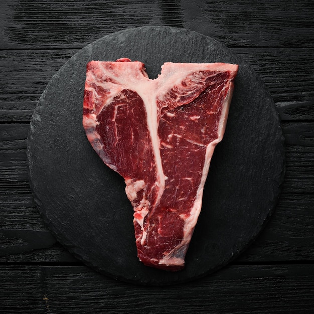 Steak Tbone cru sur une table en pierre avec du thym, du romarin et des épices Vue de dessus Vue de dessus à plat sur la table de coupe en pierre noire