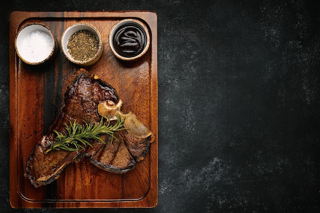 Steak de Tbone grillé succulent au romarin et épices servi sur une planche en bois sombre