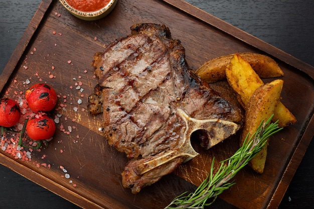 Steak de tbone sur une planche de bois avec des cueilleurs de cerises à la sauce de pommes de terre sur une table sombre