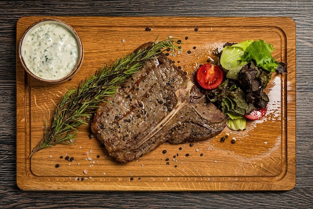 Steak de Tbone servi sur une planche de bois avec sauce légumes frais et romarin Menu du restaurant vue de dessus