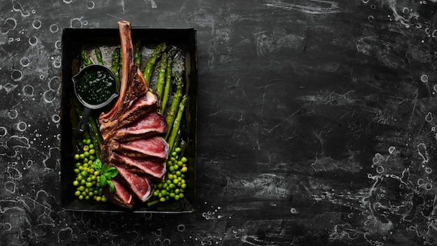 Steak Tomahawk sur l'os Steak grillé aux asperges et petits pois Sur fond noir Vue de dessus Espace de copie gratuit