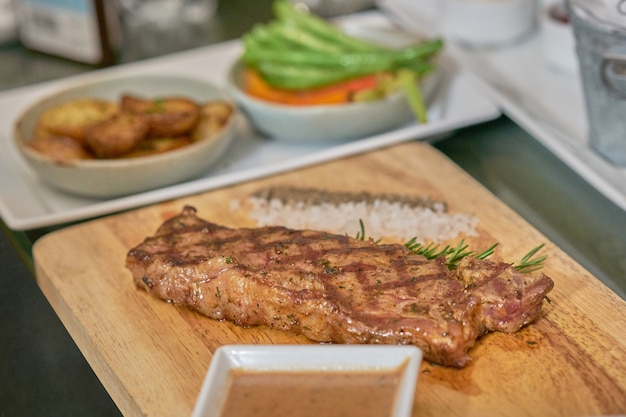 Steak avec trempette, poivre, sel et feuille de thym sur plaque de bois