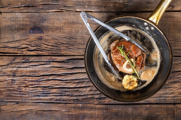 Steak de veau frit avec des assaisonnements dans une poêle à frire sur un fond en bois foncé