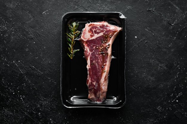 Steak de veau "New York" en emballage sous vide. Marché. Vue de dessus. Vue de dessus à plat sur la table de coupe en pierre noire.