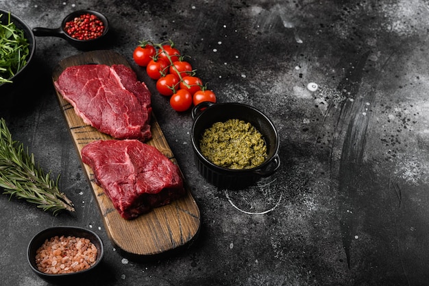 Steak de viande de boeuf cru aux herbes sur fond de table en pierre noire foncée avec espace de copie pour le texte