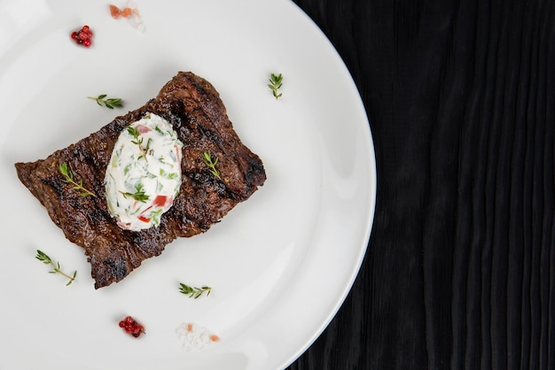 Steak de viande de boeuf jupe grillée sur une assiette avec sauce aux légumes blancs décorée d'herbes et de baies d...