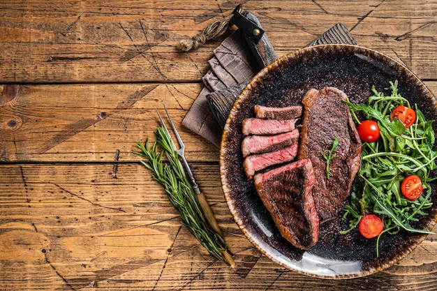 Steak de viande de boeuf rumsteck grillé au barbecue dans une assiette avec salade de légumes Fond en bois Vue de dessus Espace de copie