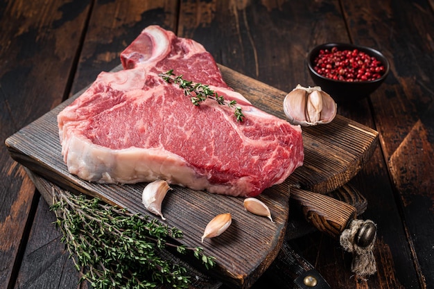 Steak de viande de bœuf Tbone Prime bifteck d'aloyau cru sur planche de boucher avec des herbes Fond en bois Vue de dessus