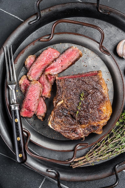 Steak de viande de bœuf Wagyu New York tranché rôti ou steak de contre-filet dans un plateau en acier avec des herbes Fond noir Vue de dessus