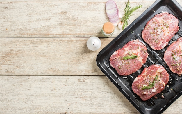 Steak de viande fraîche crue avec des feuilles de romarin et du sel sur un plateau noir prêt à être cuit, vue de dessus