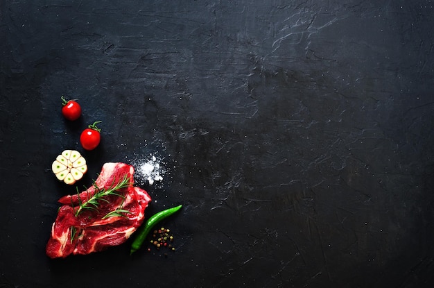 Steak de viande fraîche crue avec tomates cerises piment huile d'ail et herbes sur fond de béton en pierre sombre Espace libre pour votre texte