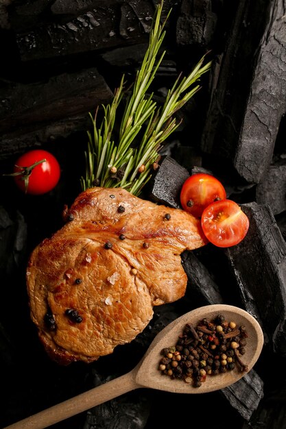 Steak de viande frite et tomates cerises poivre épicé sur fond noir de charbon de bois