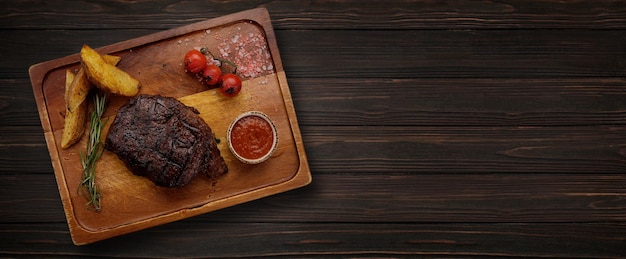 Steak de viande grillé avec pommes de terre et sauce tomate sur une planche de bois