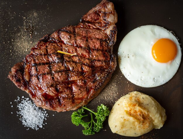 Steak de viande grillé et purée de pommes de terre avec du sel et un œuf sur une surface sombre