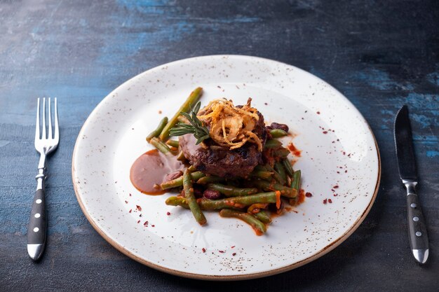 Steak de viande hachée avec sauce et chips d'oignon sur une assiette servie avec fourchette et couteau