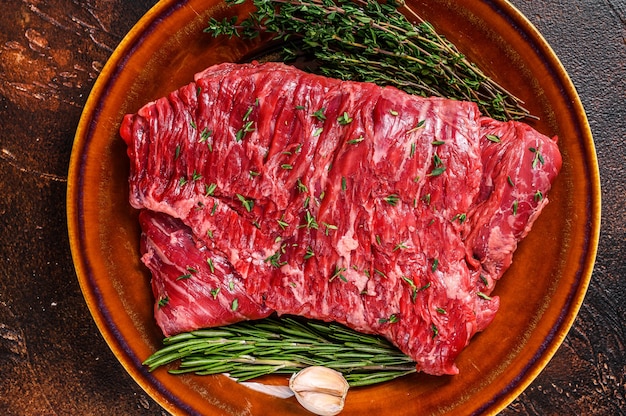 Steak de viande de jupe de boeuf cru sur une assiette rustique aux herbes. Fond sombre. Vue de dessus.