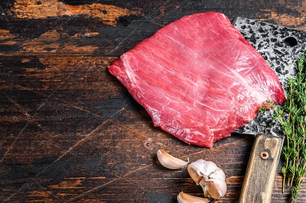 Steak de viande marbré de flanc de boeuf cru sur un couperet. Fond en bois sombre. Vue de dessus. Espace de copie.