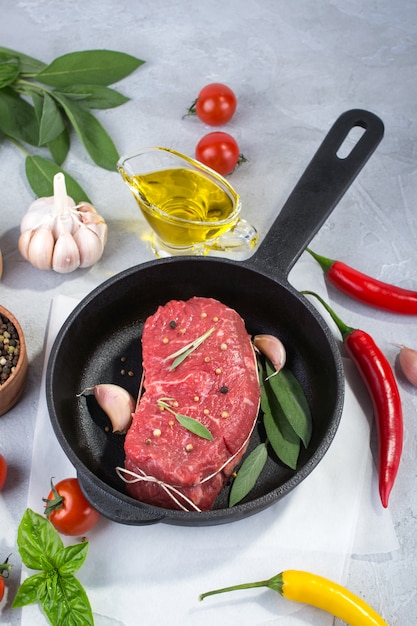 Steak de viande sur une poêle avec des ingrédients pour la cuisson sur un fond de béton gris Vue de dessus. Copiez l'espace.